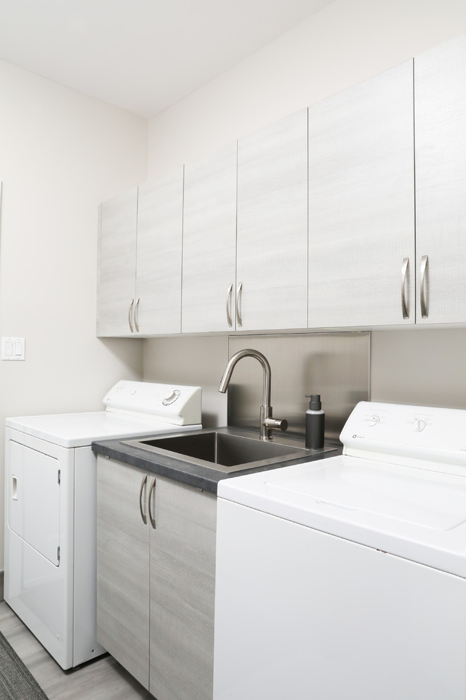 Einzeilige, Kleine Moderne Waschküche mit Einbauwaschbecken, flächenbündigen Schrankfronten, hellen Holzschränken, Laminat-Arbeitsplatte, weißer Wandfarbe, Waschmaschine und Trockner nebeneinander und grauer Arbeitsplatte in Toronto
