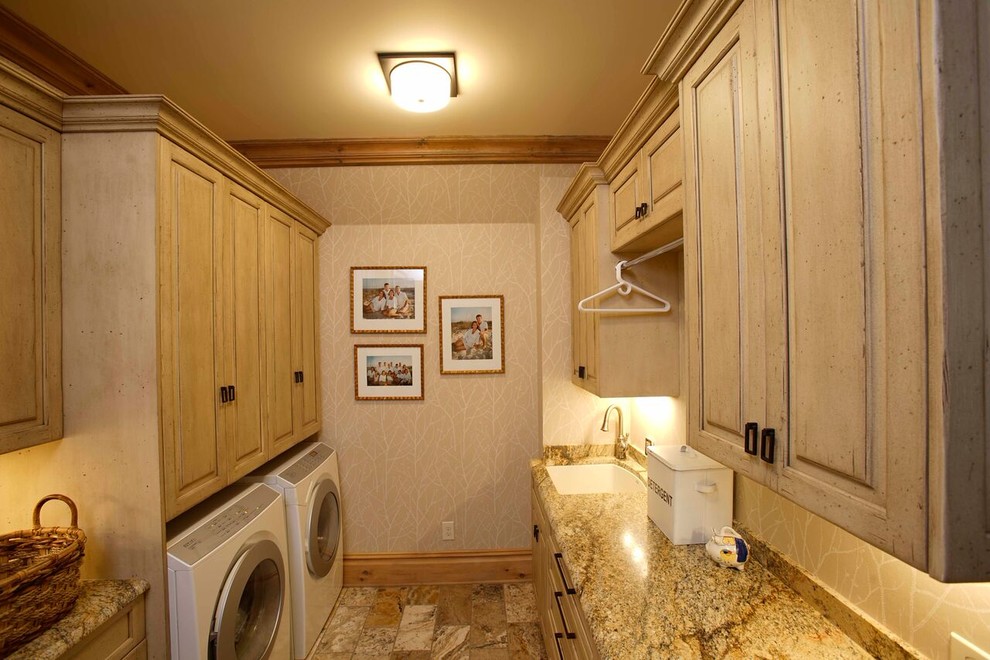 Exempel på en stor klassisk linjär tvättstuga enbart för tvätt, med beige skåp, granitbänkskiva, beige väggar, en tvättmaskin och torktumlare bredvid varandra, en undermonterad diskho och luckor med upphöjd panel