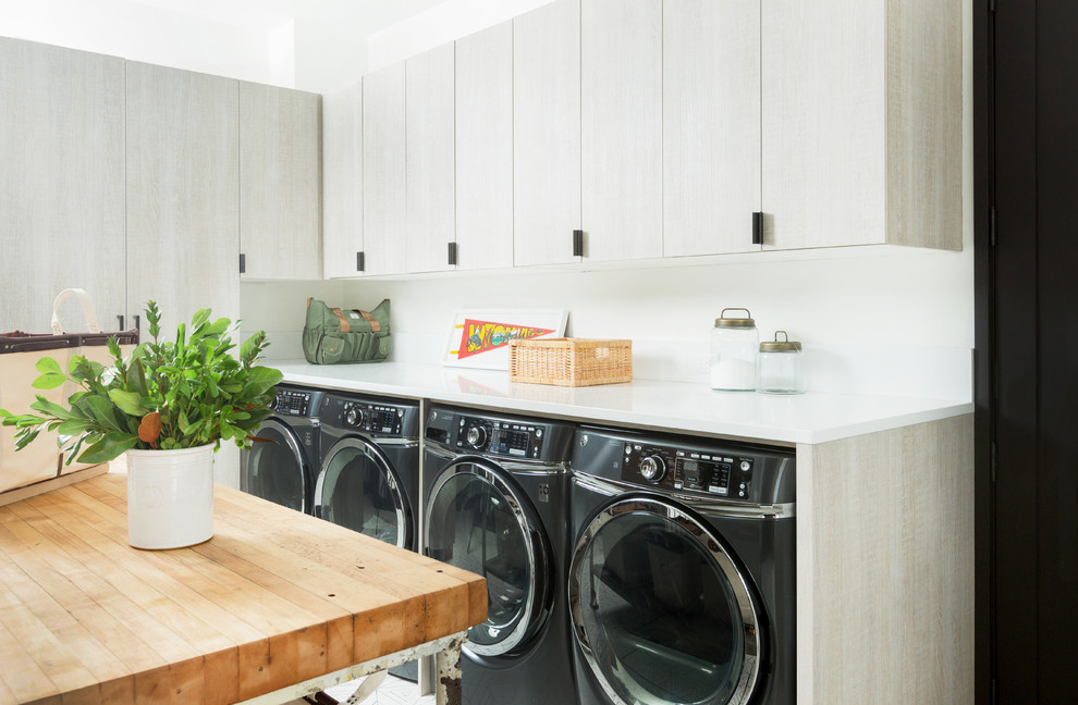 Foto på en lantlig vita l-formad tvättstuga, med släta luckor, grå skåp, vita väggar och en tvättmaskin och torktumlare bredvid varandra