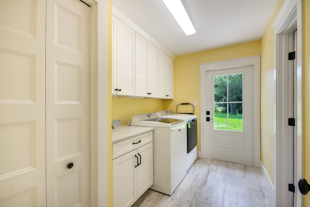 Laundry room - farmhouse galley ceramic tile and multicolored floor laundry room idea in Other with shaker cabinets, white cabinets, marble countertops, yellow walls and a side-by-side washer/dryer