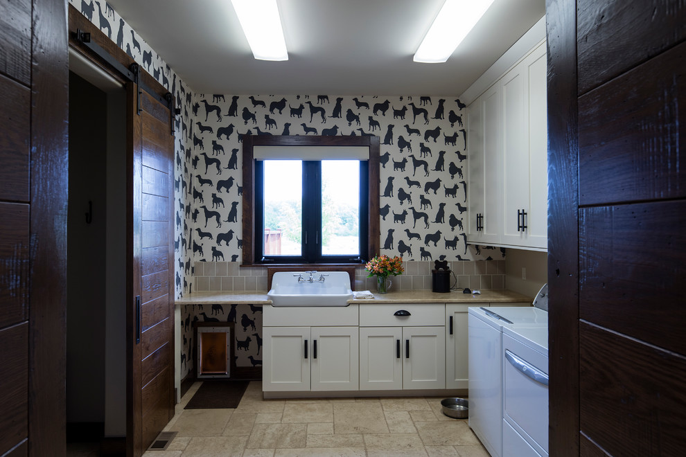 Inredning av en rustik stor l-formad tvättstuga enbart för tvätt, med en rustik diskho, skåp i shakerstil, vita skåp, bänkskiva i koppar, flerfärgade väggar, kalkstensgolv, en tvättmaskin och torktumlare bredvid varandra och beiget golv