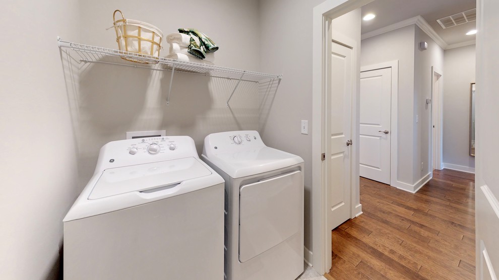 Bild på en mellanstor amerikansk linjär liten tvättstuga, med grå väggar, mellanmörkt trägolv, en tvättmaskin och torktumlare bredvid varandra och brunt golv