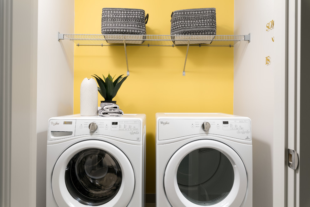 Moderner Hauswirtschaftsraum mit Waschmaschinenschrank, gelber Wandfarbe und Waschmaschine und Trockner nebeneinander in Edmonton