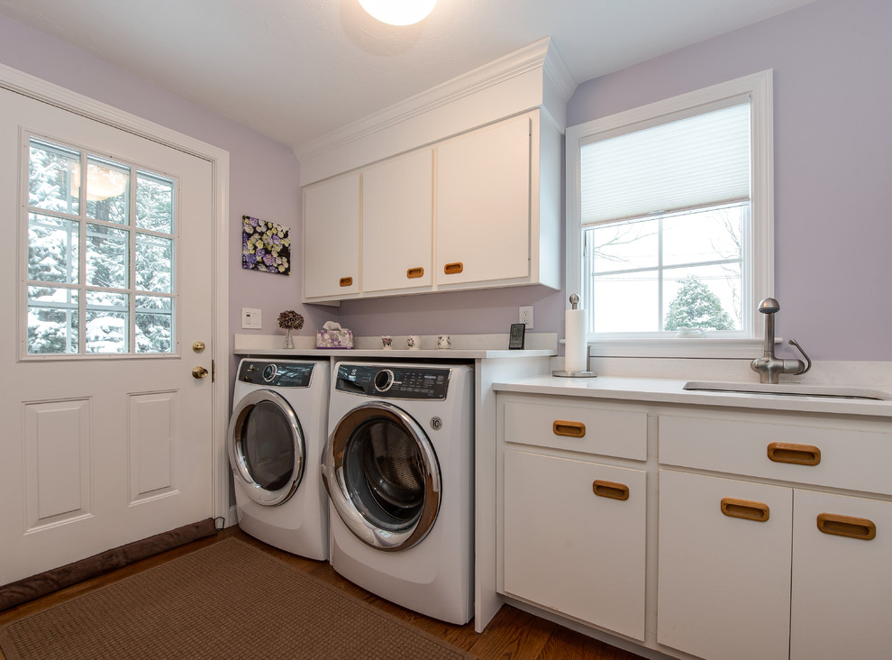 Multifunktionaler Hauswirtschaftsraum mit weißen Schränken, lila Wandfarbe, hellem Holzboden und Waschmaschine und Trockner nebeneinander in Boston