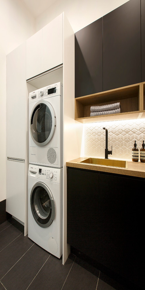 Foto di una lavanderia moderna con lavello da incasso, ante lisce, ante nere, top in laminato, pareti bianche e lavatrice e asciugatrice a colonna