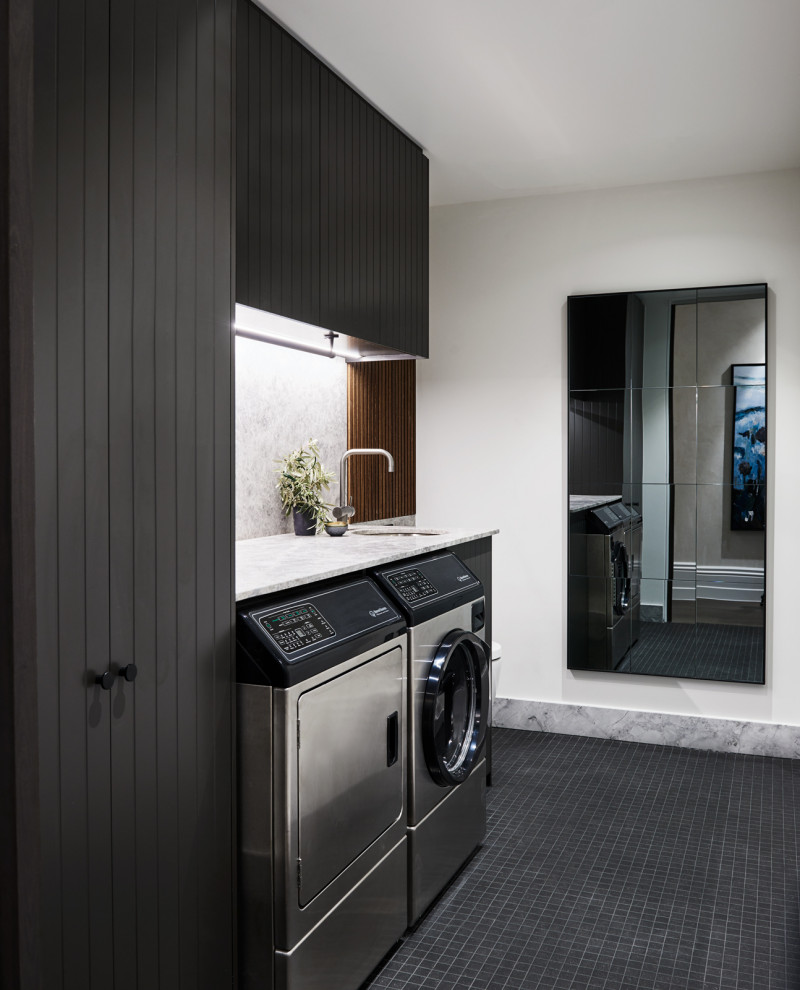 Moderne Waschküche mit Unterbauwaschbecken, schwarzen Schränken, weißer Wandfarbe, Waschmaschine und Trockner nebeneinander, schwarzem Boden und weißer Arbeitsplatte in Melbourne