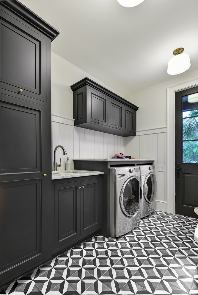 Idéer för en stor lantlig grå linjär tvättstuga enbart för tvätt, med en undermonterad diskho, luckor med infälld panel, svarta skåp, marmorbänkskiva, vita väggar, klinkergolv i porslin, en tvättmaskin och torktumlare bredvid varandra och flerfärgat golv