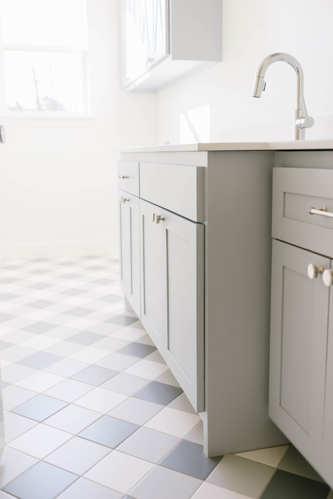 Exempel på en mellanstor lantlig vita linjär vitt tvättstuga enbart för tvätt, med en undermonterad diskho, skåp i shakerstil, blå skåp, bänkskiva i kvarts, vita väggar, klinkergolv i porslin, en tvättmaskin och torktumlare bredvid varandra och grått golv