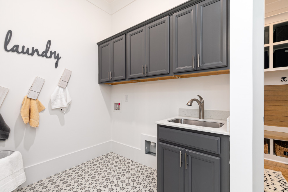 Immagine di una sala lavanderia american style di medie dimensioni con lavello da incasso, ante con bugna sagomata, ante grigie, top in quarzo composito, pareti bianche, pavimento con piastrelle in ceramica, pavimento multicolore e top bianco