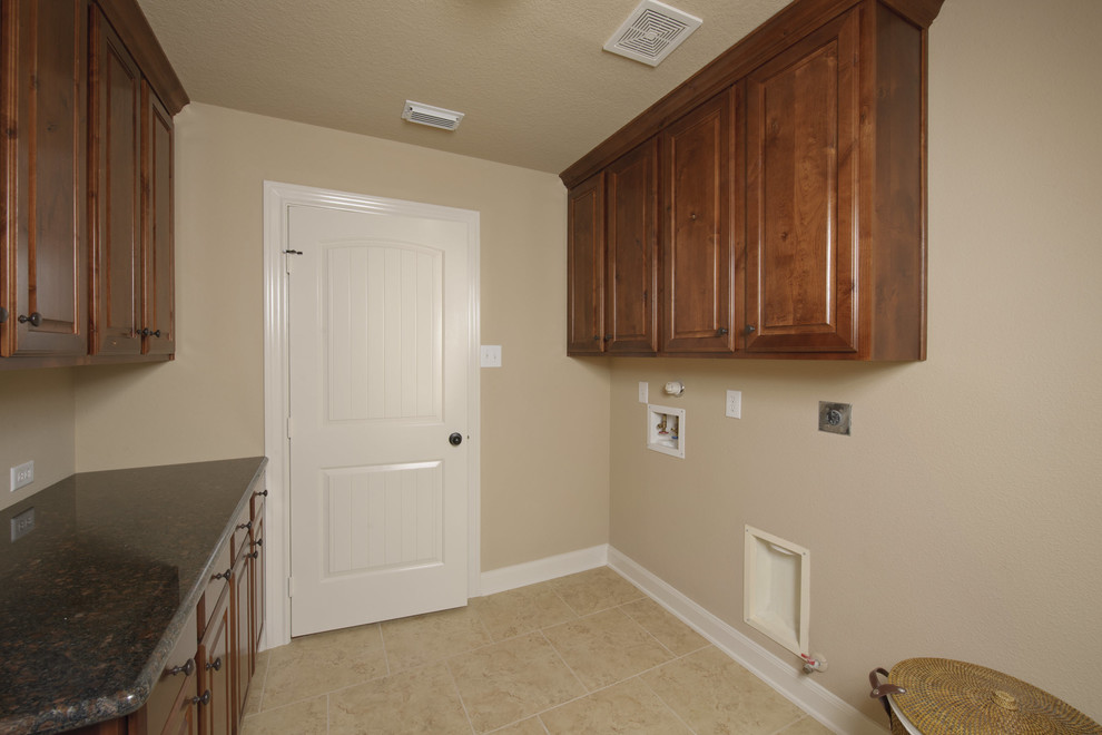 Immagine di una sala lavanderia tradizionale con ante con bugna sagomata, ante in legno bruno, top in granito, pareti beige, pavimento in gres porcellanato, pavimento beige e top nero