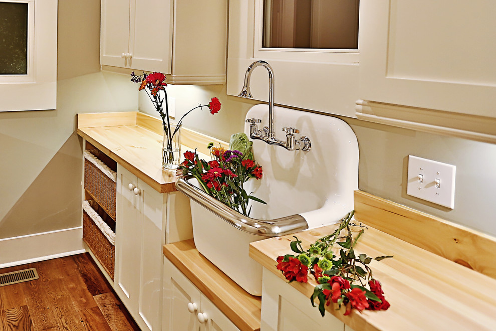 This is an example of a large farmhouse single-wall separated utility room in Nashville with a belfast sink, recessed-panel cabinets, white cabinets, wood worktops, grey walls and dark hardwood flooring.