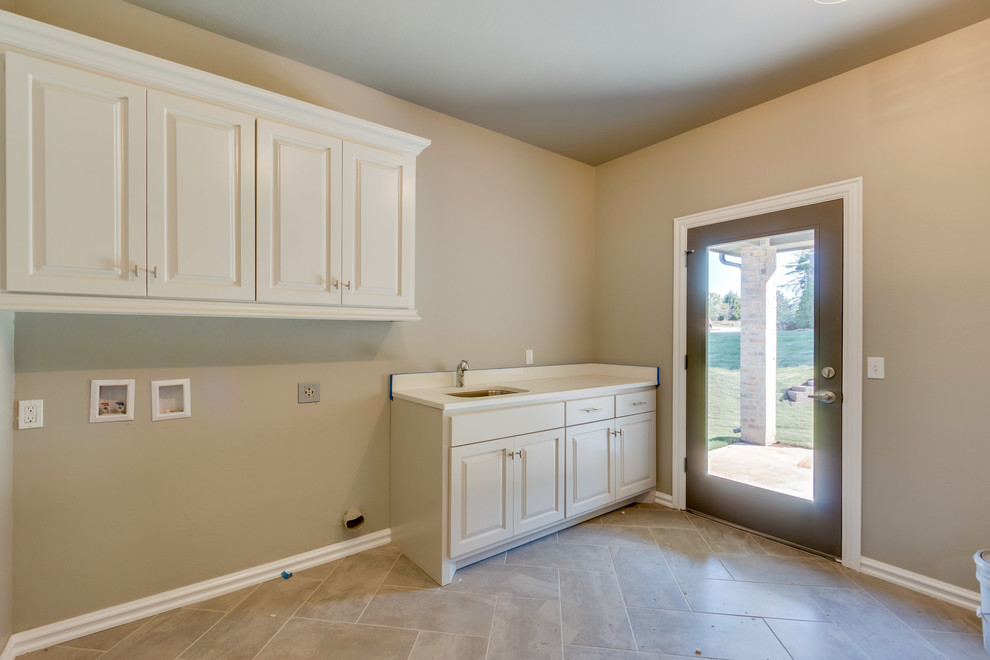 Large elegant single-wall porcelain tile utility room photo in Oklahoma City with an undermount sink, raised-panel cabinets, white cabinets, solid surface countertops, beige walls and a side-by-side washer/dryer