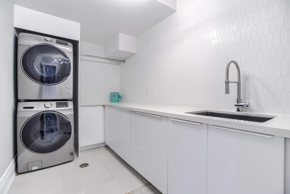トロントにある高級な中くらいなトランジショナルスタイルのおしゃれな洗濯室 (L型、アンダーカウンターシンク、フラットパネル扉のキャビネット、白いキャビネット、クオーツストーンカウンター、白いキッチンパネル、磁器タイルのキッチンパネル、白い壁、クッションフロア、上下配置の洗濯機・乾燥機、白い床、白いキッチンカウンター) の写真