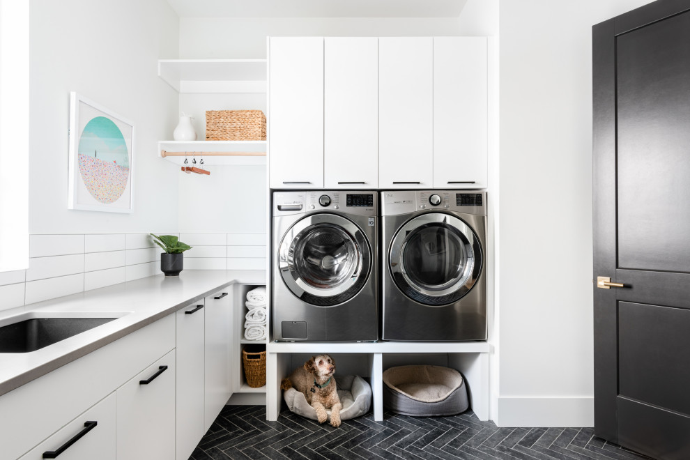This is an example of a modern l-shaped utility room in Vancouver with a submerged sink, flat-panel cabinets, engineered stone countertops, white splashback, engineered quartz splashback, white worktops, white cabinets, white walls, ceramic flooring, a side by side washer and dryer and grey floors.