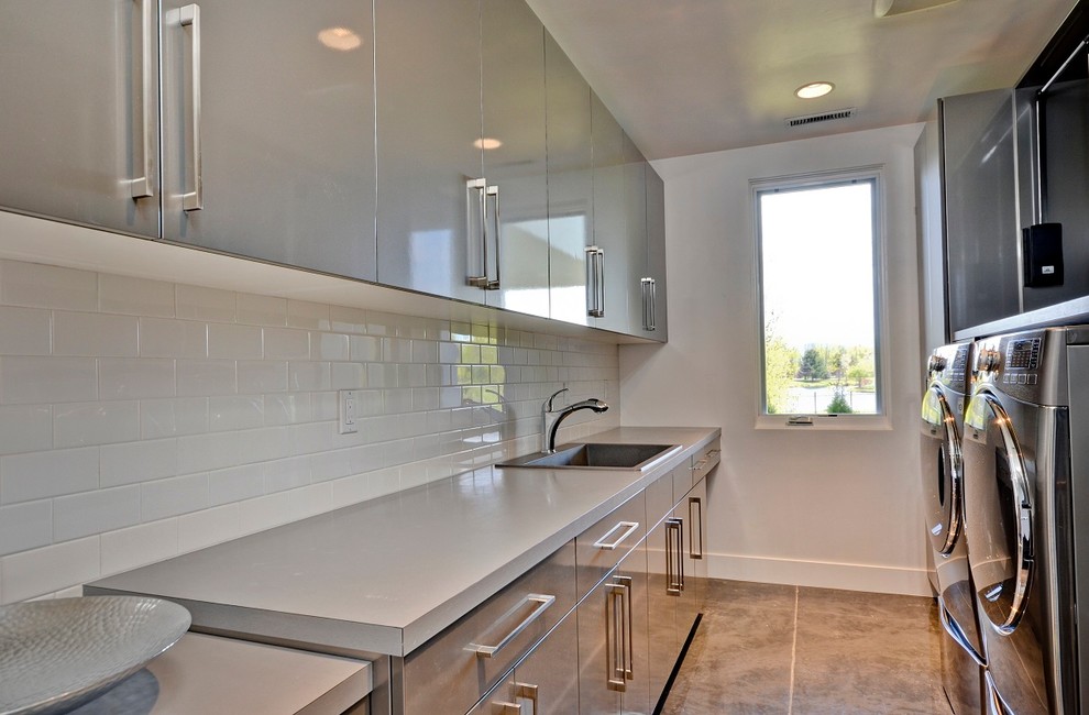 Contemporary utility room in Boise with flat-panel cabinets, grey cabinets, a side by side washer and dryer, a built-in sink, laminate countertops, white walls, concrete flooring and grey worktops.