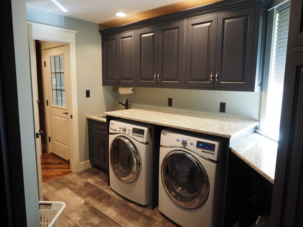 Inredning av en amerikansk linjär tvättstuga enbart för tvätt, med en allbänk, luckor med profilerade fronter, blå skåp, granitbänkskiva, gröna väggar, klinkergolv i keramik och en tvättmaskin och torktumlare bredvid varandra