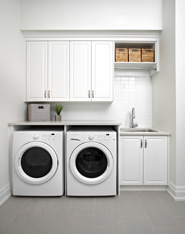 Imagen de lavadero lineal clásico con fregadero bajoencimera, armarios con paneles con relieve, puertas de armario blancas, paredes blancas, lavadora y secadora juntas y encimeras grises