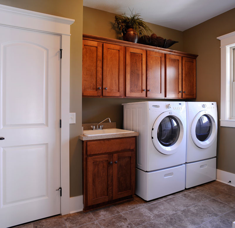 Inspiration for a rustic single-wall utility room with an utility sink, shaker cabinets, medium wood cabinets, beige walls and a side by side washer and dryer.
