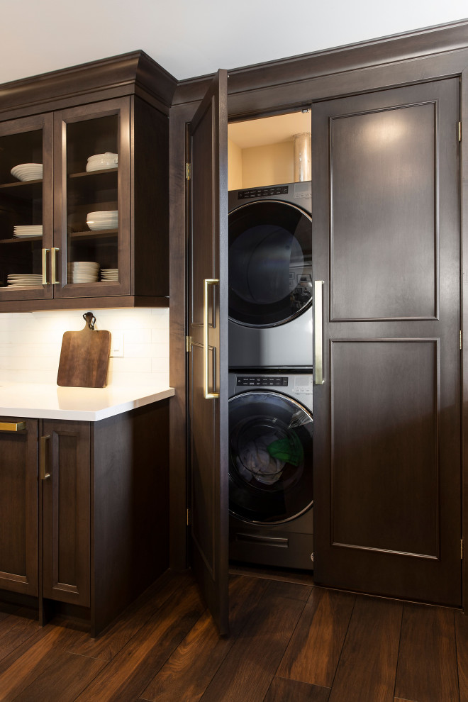 Inspiration for a small timeless single-wall dark wood floor and brown floor laundry closet remodel in Toronto with recessed-panel cabinets, dark wood cabinets, quartz countertops, gray walls, a stacked washer/dryer and white countertops