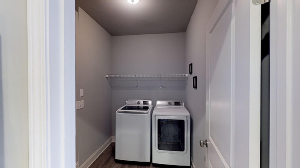 Ejemplo de armario lavadero de estilo americano de tamaño medio con paredes grises, suelo de madera oscura, lavadora y secadora juntas y suelo marrón