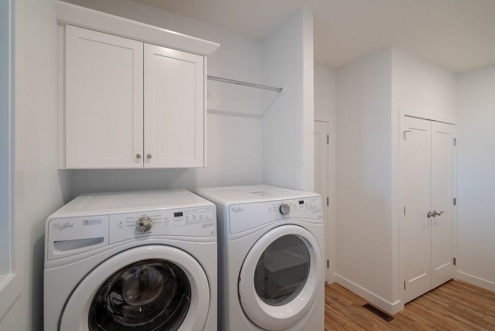 Design ideas for a medium sized classic utility room in Other with an utility sink, white cabinets, white walls, medium hardwood flooring, a side by side washer and dryer and brown floors.