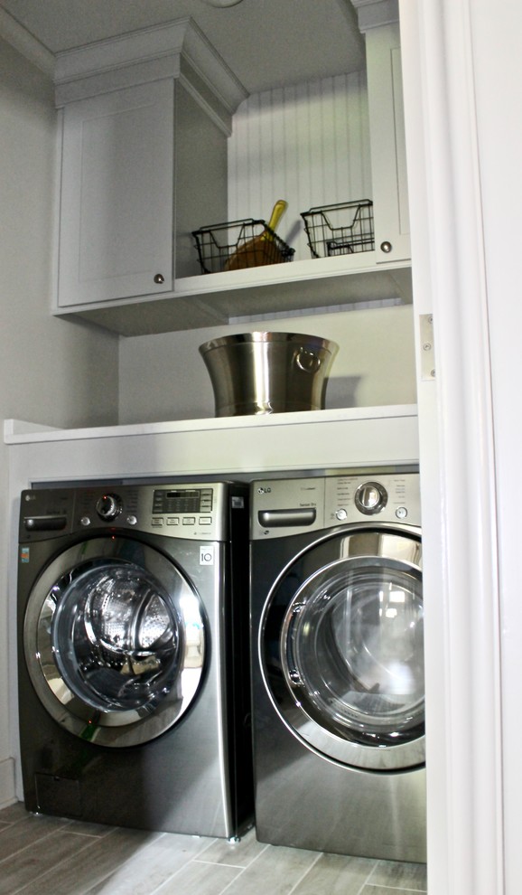 Inredning av en klassisk mellanstor vita linjär vitt tvättstuga enbart för tvätt, med skåp i shakerstil, vita skåp, grå väggar, ljust trägolv, en tvättmaskin och torktumlare bredvid varandra och flerfärgat golv