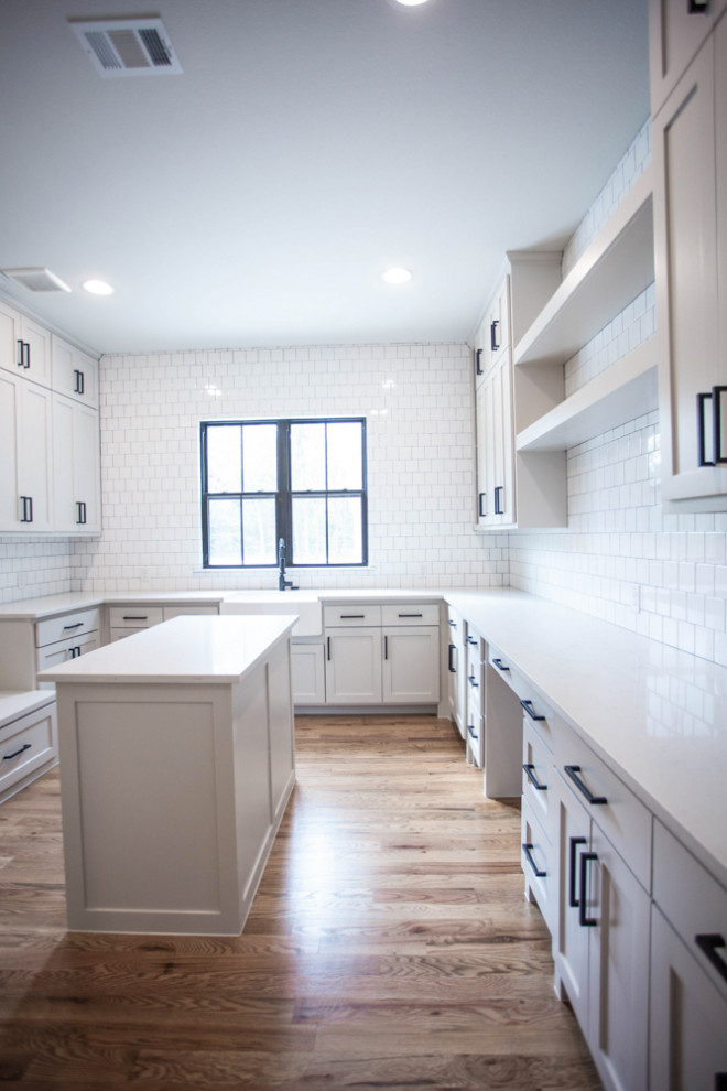 This is an example of a large country u-shaped separated utility room in Dallas with a belfast sink, shaker cabinets, white cabinets, quartz worktops, white walls, light hardwood flooring, a side by side washer and dryer, beige floors and white worktops.