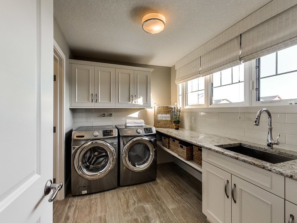 Exempel på en klassisk linjär tvättstuga enbart för tvätt, med en undermonterad diskho, vita skåp, grå väggar, mellanmörkt trägolv, en tvättmaskin och torktumlare bredvid varandra och luckor med infälld panel