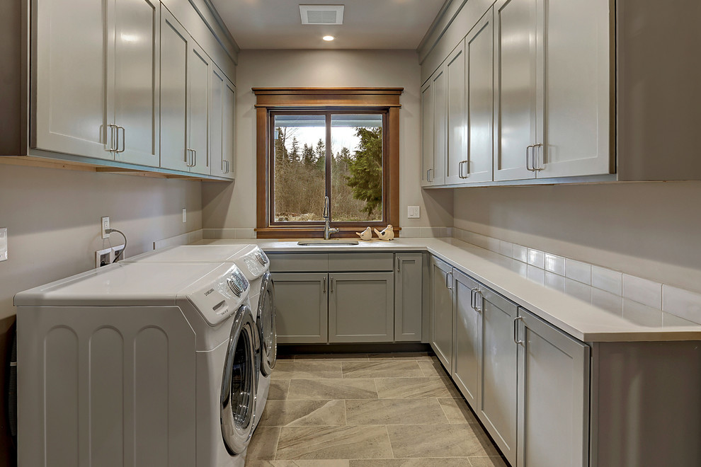 Großer Klassischer Hauswirtschaftsraum in U-Form mit Waschbecken, Schrankfronten im Shaker-Stil, grauen Schränken, beiger Wandfarbe, Porzellan-Bodenfliesen, Waschmaschine und Trockner nebeneinander und weißer Arbeitsplatte in Seattle