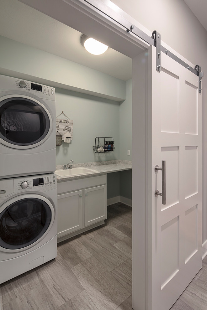 Foto på en linjär tvättstuga enbart för tvätt, med en nedsänkt diskho, luckor med infälld panel, vita skåp, bänkskiva i kvarts, gröna väggar, vinylgolv, en tvättpelare och grått golv