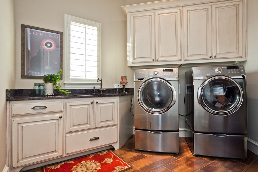 ダラスにあるトラディショナルスタイルのおしゃれな洗濯室 (レイズドパネル扉のキャビネット、ベージュのキャビネット、ベージュの壁、左右配置の洗濯機・乾燥機、オレンジの床) の写真