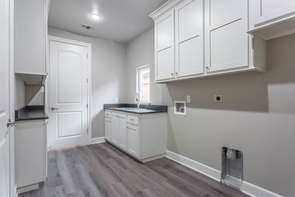 This is an example of a medium sized traditional galley utility room in Austin with a built-in sink, shaker cabinets, white cabinets, grey walls, dark hardwood flooring, a side by side washer and dryer, brown floors and black worktops.