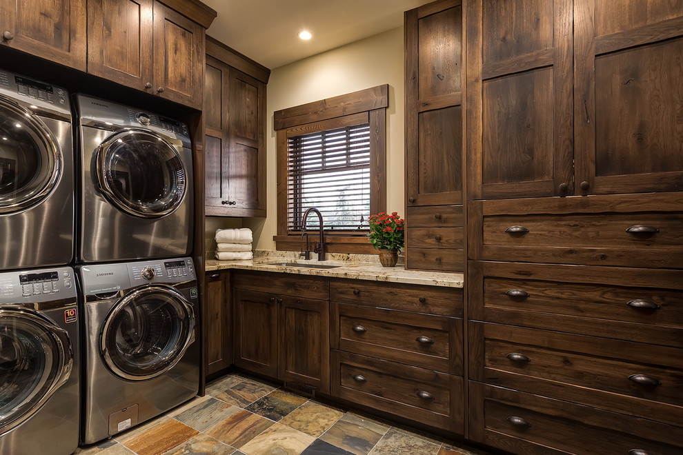 Inspiration for a large rustic l-shaped separated utility room in Calgary with a submerged sink, shaker cabinets, dark wood cabinets, granite worktops, slate flooring, a stacked washer and dryer, beige walls and beige worktops.