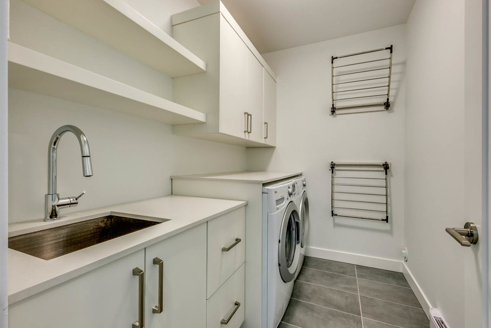 Esempio di una sala lavanderia minimalista di medie dimensioni con lavello sottopiano, ante lisce, ante bianche, pareti bianche, pavimento in ardesia, lavatrice e asciugatrice affiancate e pavimento grigio