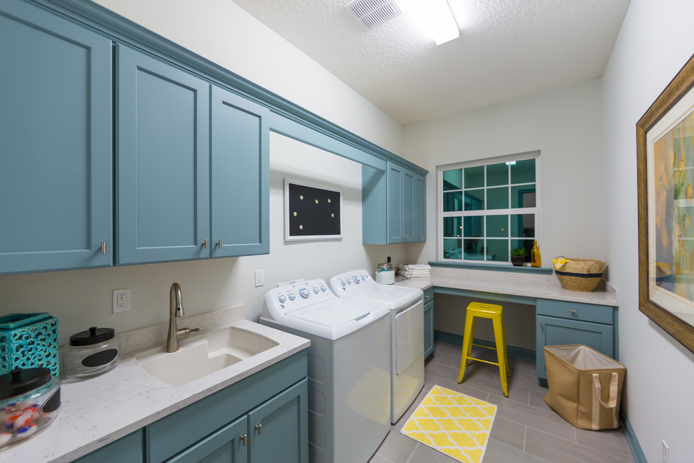Photo of a large classic l-shaped separated utility room in Jacksonville with a submerged sink, shaker cabinets, blue cabinets, a side by side washer and dryer, engineered stone countertops, grey walls, ceramic flooring and white worktops.