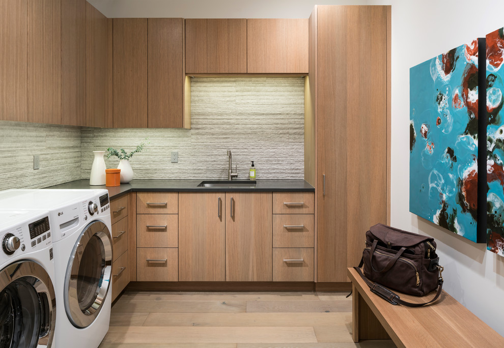 Immagine di una sala lavanderia design con lavello sottopiano, ante lisce, ante in legno scuro, pareti bianche, parquet chiaro, lavatrice e asciugatrice affiancate, pavimento beige e top grigio