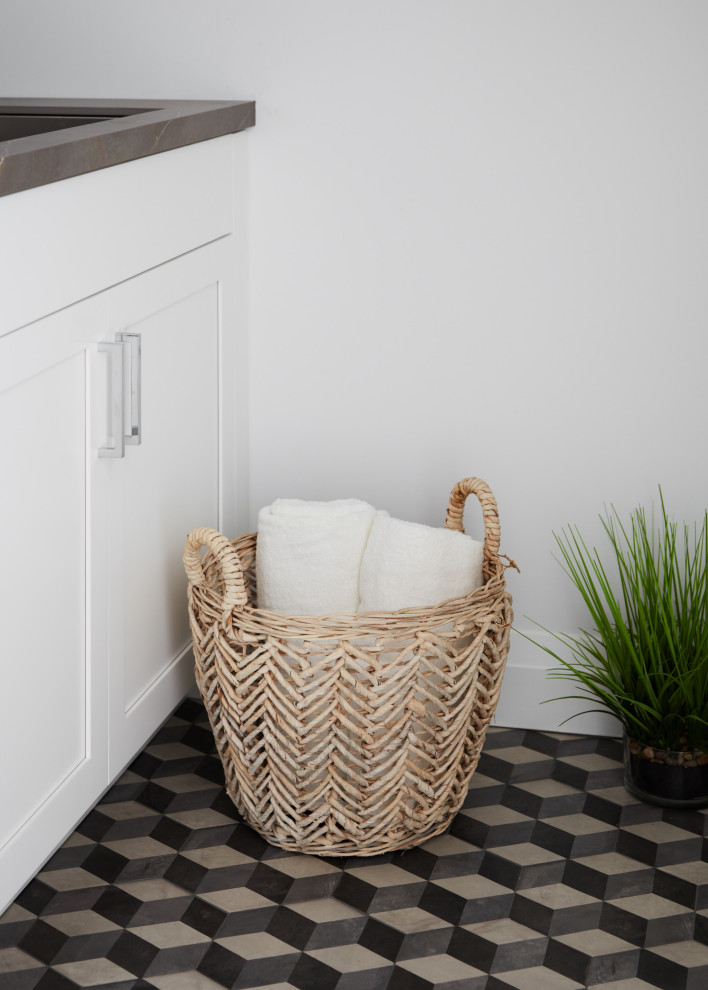 Inredning av en klassisk liten grå linjär grått tvättstuga enbart för tvätt, med en undermonterad diskho, vita skåp, vita väggar, klinkergolv i porslin, en tvättmaskin och torktumlare bredvid varandra och flerfärgat golv