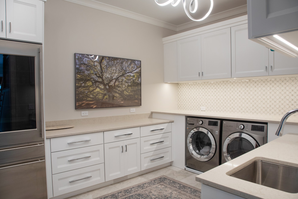 Photo of a large nautical u-shaped separated utility room in Milwaukee with a submerged sink, recessed-panel cabinets, white cabinets, engineered stone countertops, beige splashback, porcelain splashback, beige walls, porcelain flooring, a side by side washer and dryer, beige floors and beige worktops.