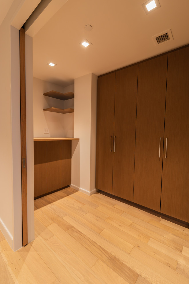 Modern utility room in New York with light wood cabinets, wood worktops, white walls, light hardwood flooring, a concealed washer and dryer and yellow floors.