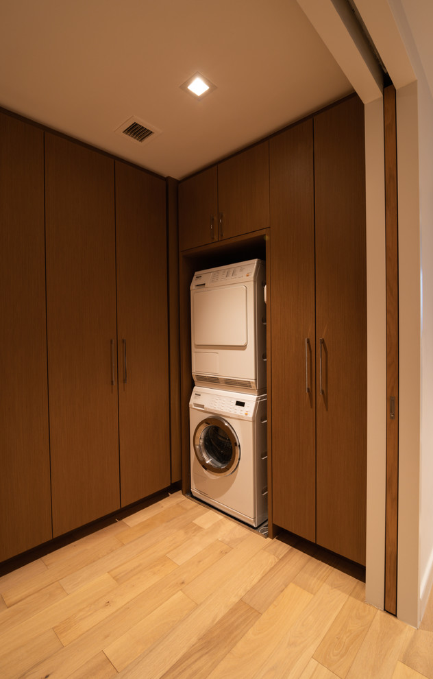 Diseño de lavadero minimalista con puertas de armario de madera clara, encimera de madera, paredes blancas, suelo de madera clara, lavadora y secadora escondidas y suelo amarillo