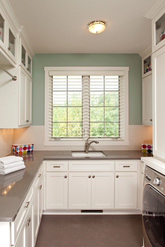 Modelo de lavadero clásico con paredes verdes, puertas de armario blancas, suelo marrón y encimeras grises