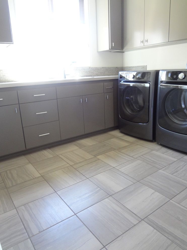 Idéer för mellanstora funkis l-formade tvättstugor enbart för tvätt, med en undermonterad diskho, släta luckor, grå skåp, bänkskiva i kvartsit, vita väggar, klinkergolv i keramik och en tvättmaskin och torktumlare bredvid varandra