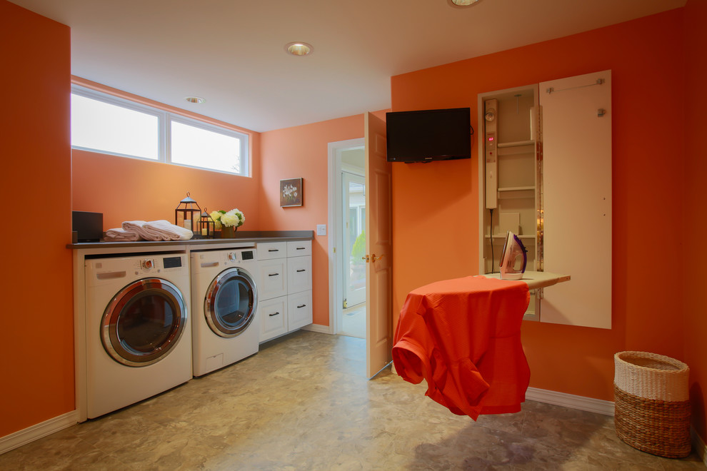 Bild på ett vintage linjärt grovkök, med släta luckor, vita skåp, orange väggar, en tvättmaskin och torktumlare bredvid varandra och betonggolv