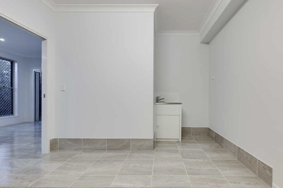 На фото: универсальная комната среднего размера в стиле модернизм с хозяйственной раковиной, белыми стенами, полом из керамогранита и серым полом с