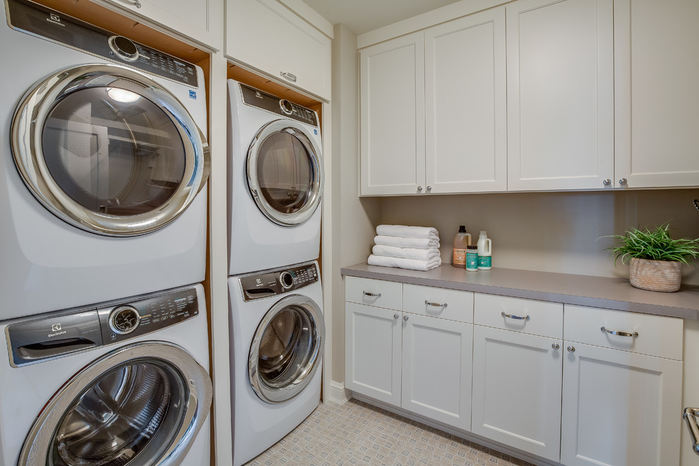 ミネアポリスにあるトラディショナルスタイルのおしゃれな洗濯室 (シェーカースタイル扉のキャビネット、白いキャビネット、グレーの壁、上下配置の洗濯機・乾燥機、ベージュの床、グレーのキッチンカウンター) の写真