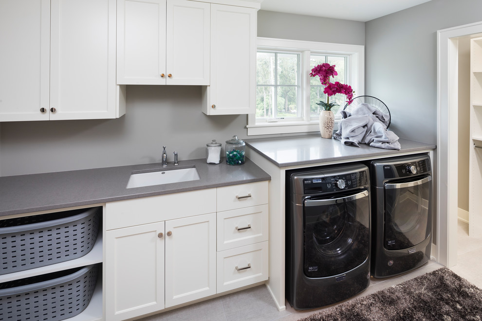 This is an example of a medium sized traditional utility room in Minneapolis with a built-in sink, white cabinets, engineered stone countertops, grey walls, a side by side washer and dryer and grey floors.
