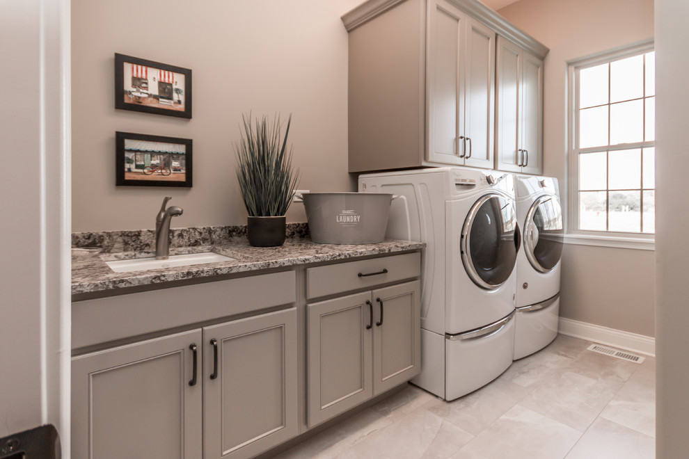 Exempel på en mellanstor klassisk grå linjär grått tvättstuga enbart för tvätt, med en undermonterad diskho, släta luckor, beige skåp, granitbänkskiva, beige väggar, klinkergolv i porslin, en tvättmaskin och torktumlare bredvid varandra och beiget golv