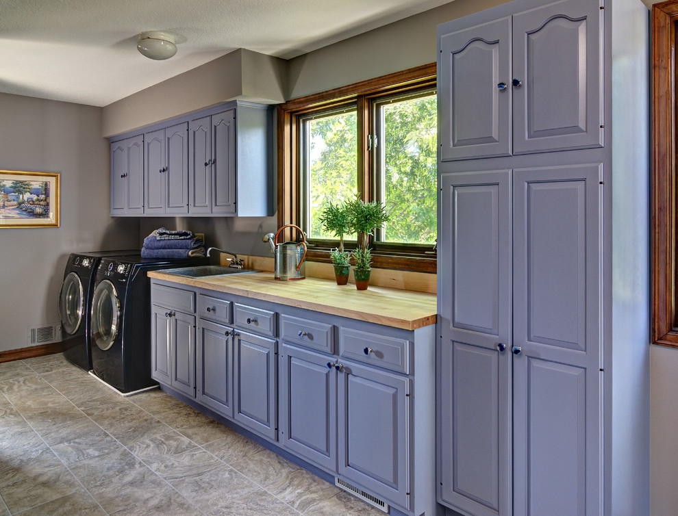 Photo of a medium sized classic single-wall separated utility room in Minneapolis with a built-in sink, raised-panel cabinets, blue cabinets, wood worktops, grey walls, ceramic flooring and a side by side washer and dryer.