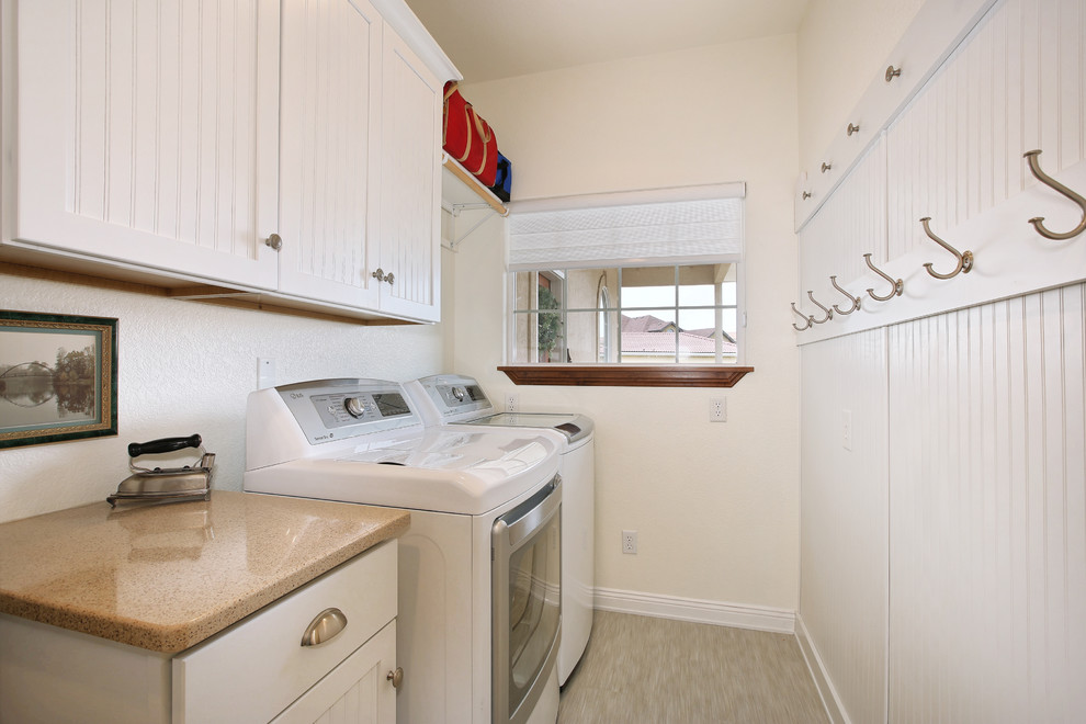Exempel på en mellanstor klassisk linjär tvättstuga enbart för tvätt, med luckor med profilerade fronter, vita skåp, vita väggar, ljust trägolv, en tvättmaskin och torktumlare bredvid varandra, beiget golv och bänkskiva i kvarts