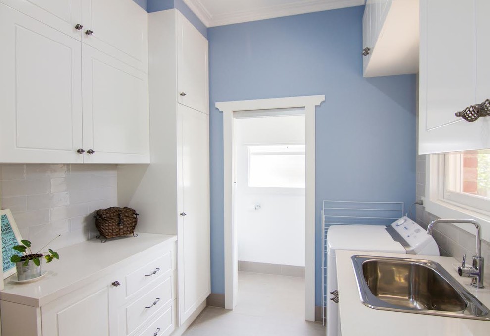 Esempio di una sala lavanderia classica di medie dimensioni con lavello a vasca singola, ante in stile shaker, ante bianche, top in granito, pareti blu, pavimento in travertino, pavimento beige e lavasciuga